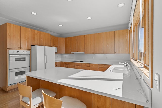 kitchen featuring a kitchen bar, light countertops, a peninsula, white appliances, and a sink