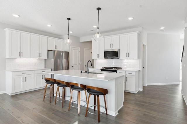 kitchen with an island with sink, wood finished floors, appliances with stainless steel finishes, and a sink