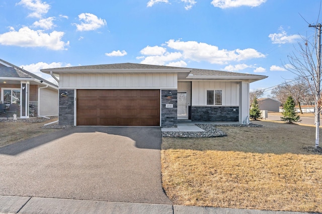 view of front facade with a front lawn, aphalt driveway, stone siding, board and batten siding, and a garage