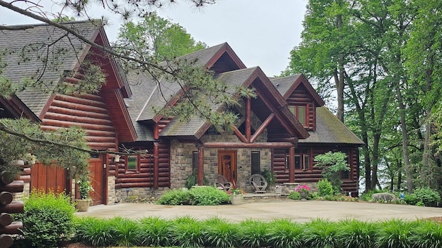 cabin with concrete driveway, log siding, stone siding, and a shingled roof