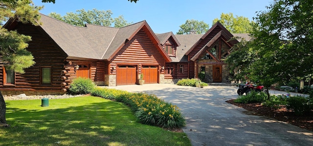 cabin featuring driveway, log siding, an attached garage, a front lawn, and stone siding