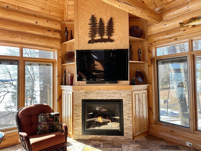 living room featuring a glass covered fireplace, a healthy amount of sunlight, and rustic walls