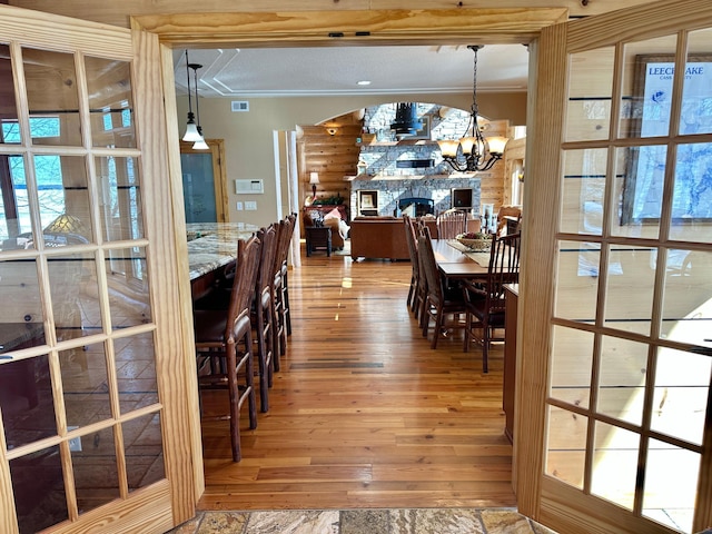 dining room with visible vents, light wood finished floors, an inviting chandelier, arched walkways, and a stone fireplace