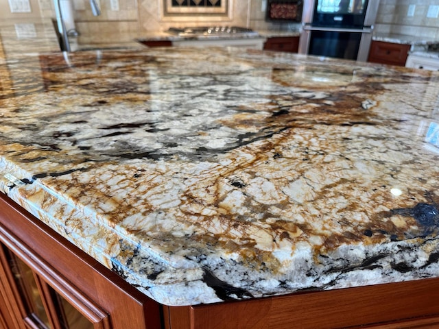 details featuring light stone counters, double oven, and brown cabinetry