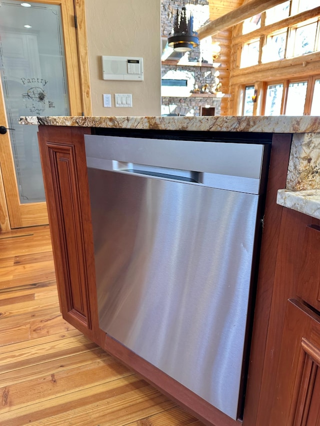 interior details with rustic walls, light wood-type flooring, light stone countertops, and stainless steel dishwasher