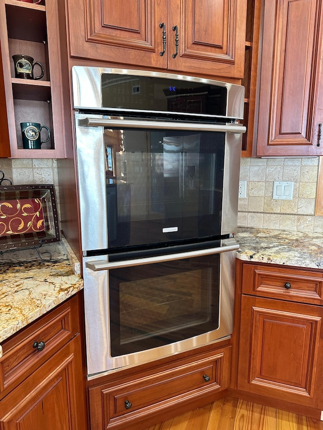 kitchen featuring double oven, light stone counters, tasteful backsplash, and brown cabinets