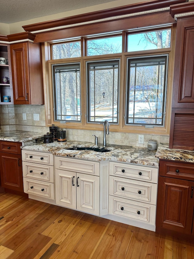 kitchen with brown cabinetry, light stone countertops, a sink, decorative backsplash, and light wood-type flooring