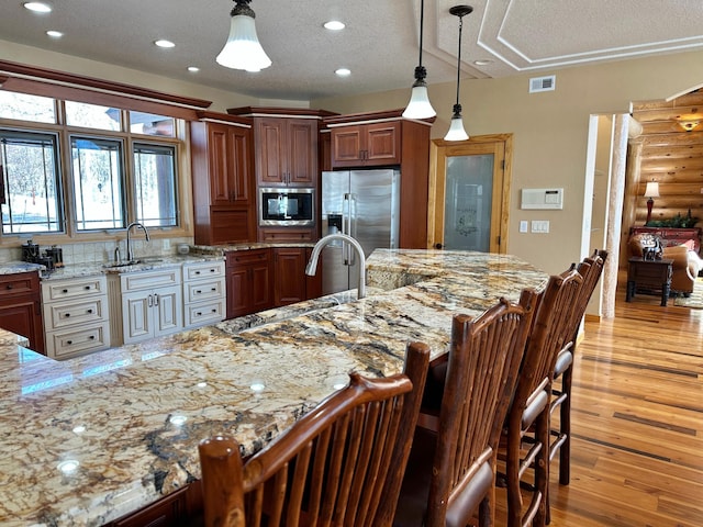 kitchen featuring light wood-style flooring, decorative light fixtures, stainless steel appliances, a breakfast bar area, and light stone countertops