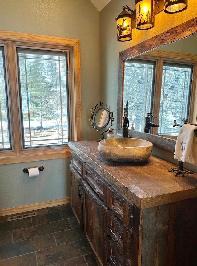 bathroom featuring visible vents, stone finish floor, baseboards, vanity, and a textured wall