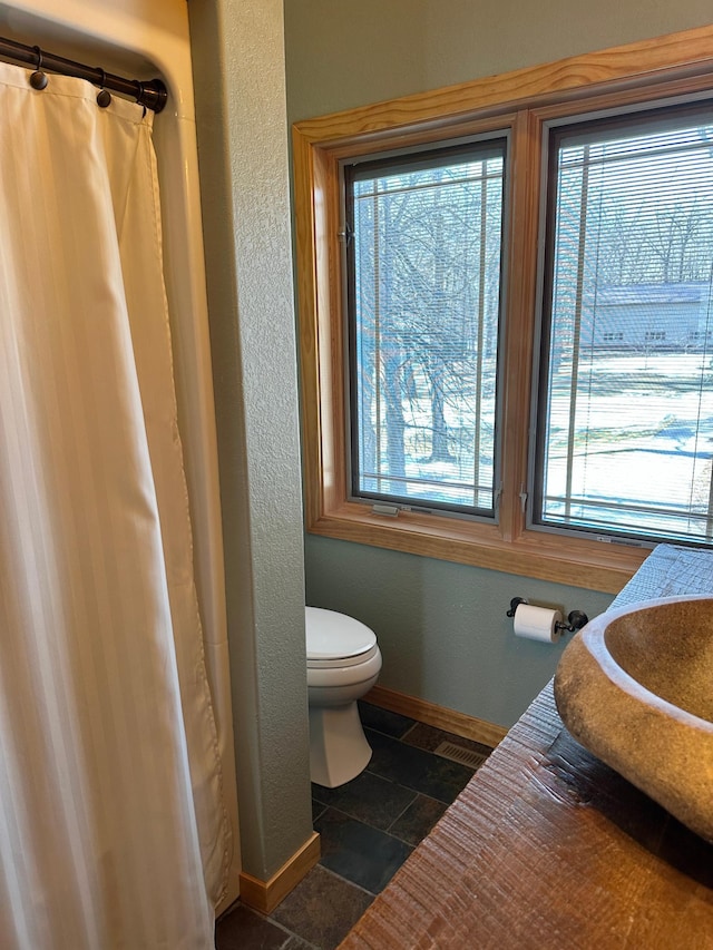 full bathroom featuring a shower with shower curtain, toilet, baseboards, and stone tile flooring