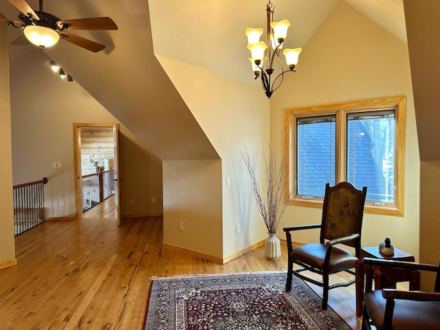 living area featuring ceiling fan with notable chandelier, vaulted ceiling, wood finished floors, and baseboards