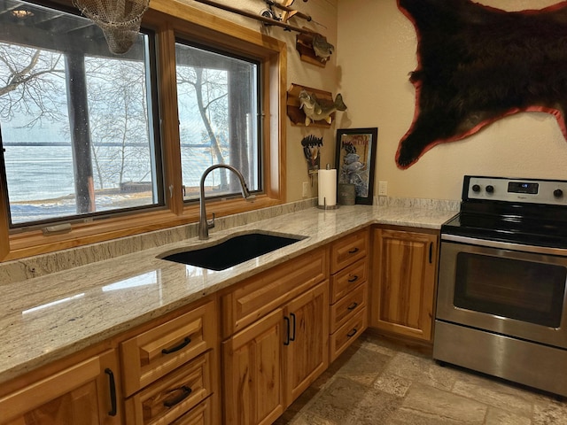 kitchen featuring a sink, stone finish flooring, brown cabinetry, stainless steel electric range oven, and light stone countertops