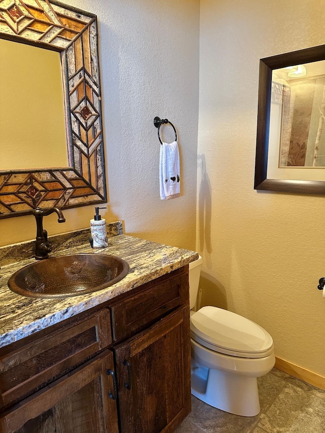 half bath with vanity, toilet, a textured wall, and baseboards