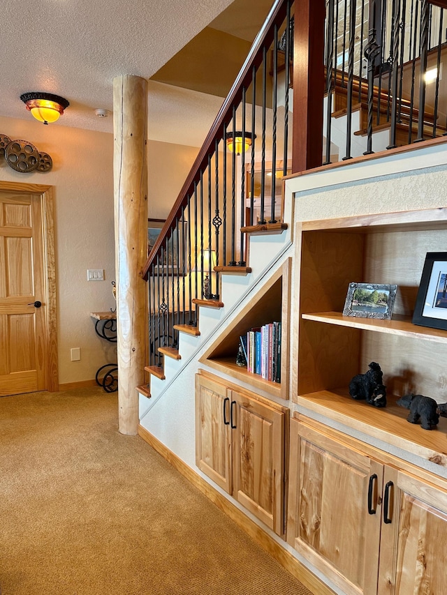 staircase featuring a textured ceiling, baseboards, and carpet floors