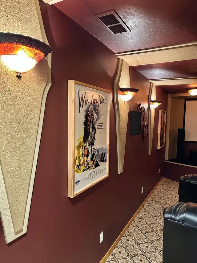 hallway featuring visible vents, baseboards, a textured ceiling, and carpet flooring