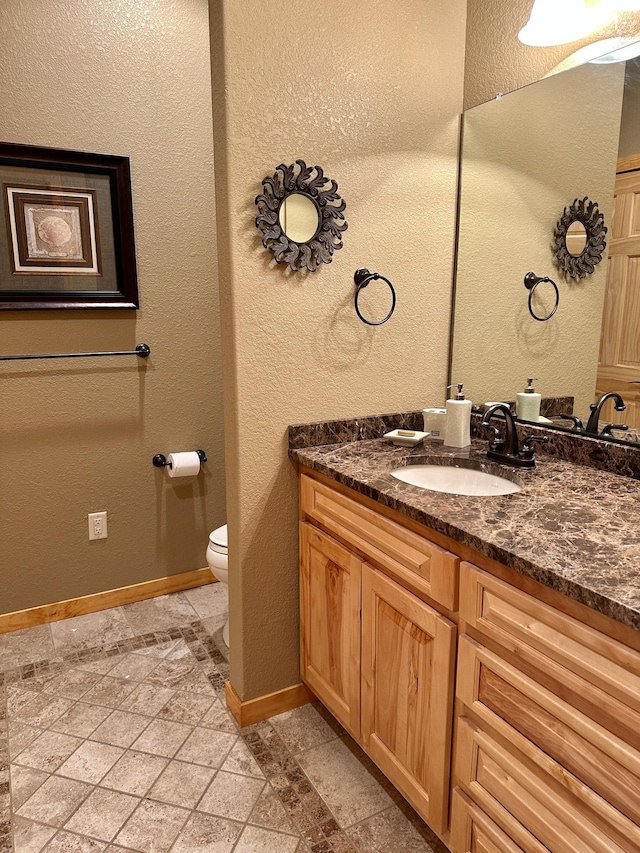 bathroom featuring stone tile flooring, toilet, vanity, and baseboards