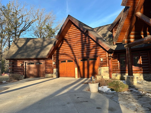 view of property exterior with log exterior, a garage, roof with shingles, and concrete driveway