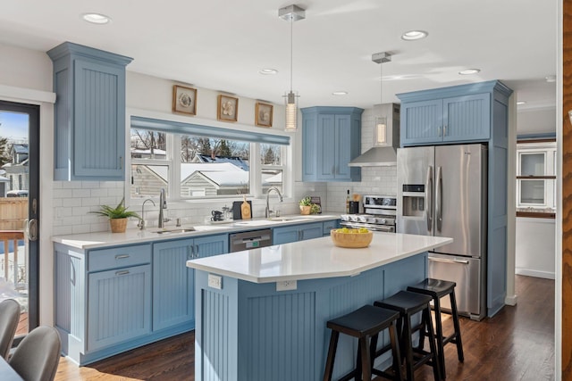 kitchen featuring blue cabinetry, appliances with stainless steel finishes, wall chimney range hood, and a sink