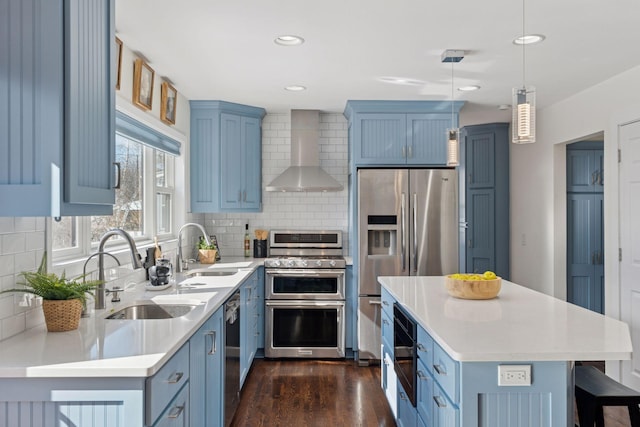 kitchen featuring blue cabinetry, stainless steel appliances, a sink, and wall chimney range hood