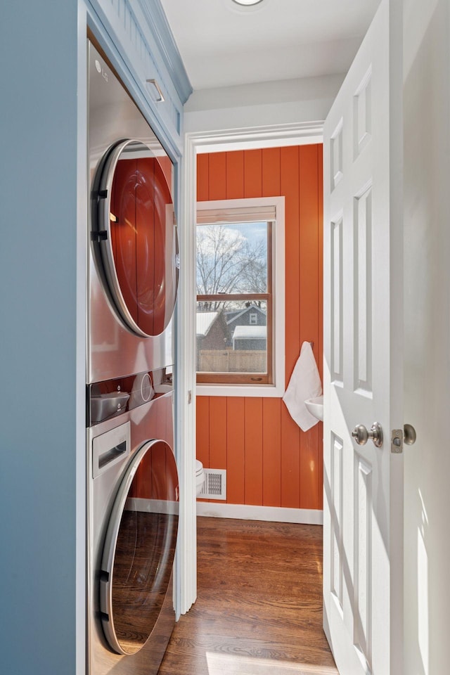 clothes washing area with laundry area, stacked washer / drying machine, visible vents, and wood finished floors