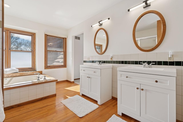 full bath with visible vents, two vanities, a sink, wood finished floors, and tile walls