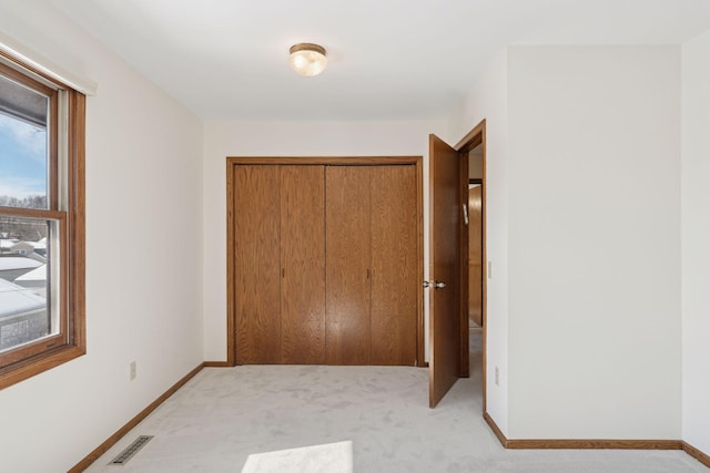 unfurnished bedroom with a closet, visible vents, light carpet, and baseboards