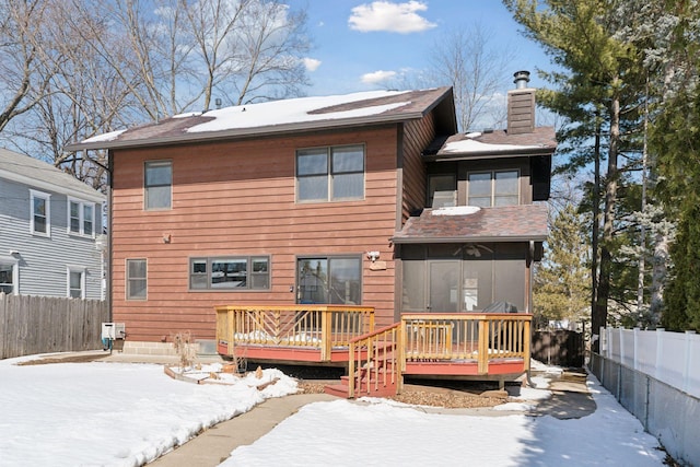 snow covered back of property featuring a deck, a fenced backyard, and a chimney