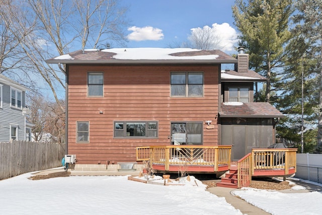 snow covered back of property featuring a fenced backyard, a chimney, and a wooden deck