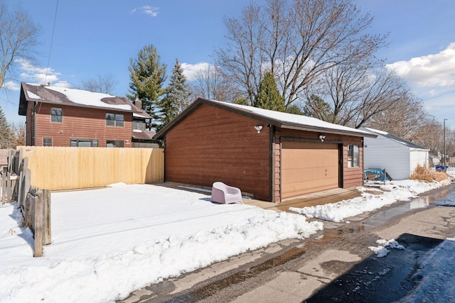 view of snow covered exterior with a detached garage, an outdoor structure, and fence