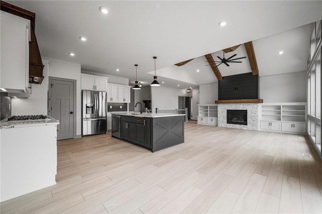 kitchen featuring lofted ceiling with beams, white cabinets, hanging light fixtures, a kitchen island with sink, and stainless steel appliances