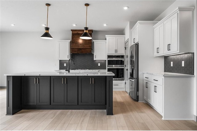 kitchen with light hardwood / wood-style flooring, hanging light fixtures, stainless steel appliances, an island with sink, and white cabinets