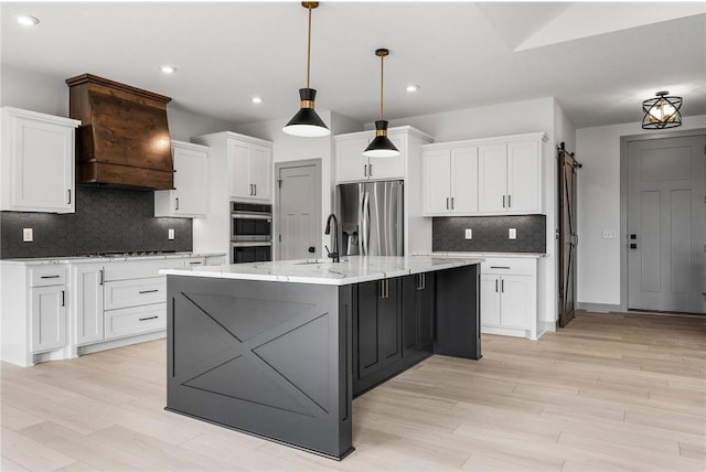 kitchen with appliances with stainless steel finishes, sink, white cabinets, hanging light fixtures, and a kitchen island with sink