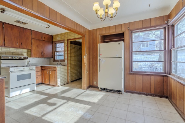 kitchen featuring wood walls, an inviting chandelier, decorative light fixtures, white appliances, and backsplash