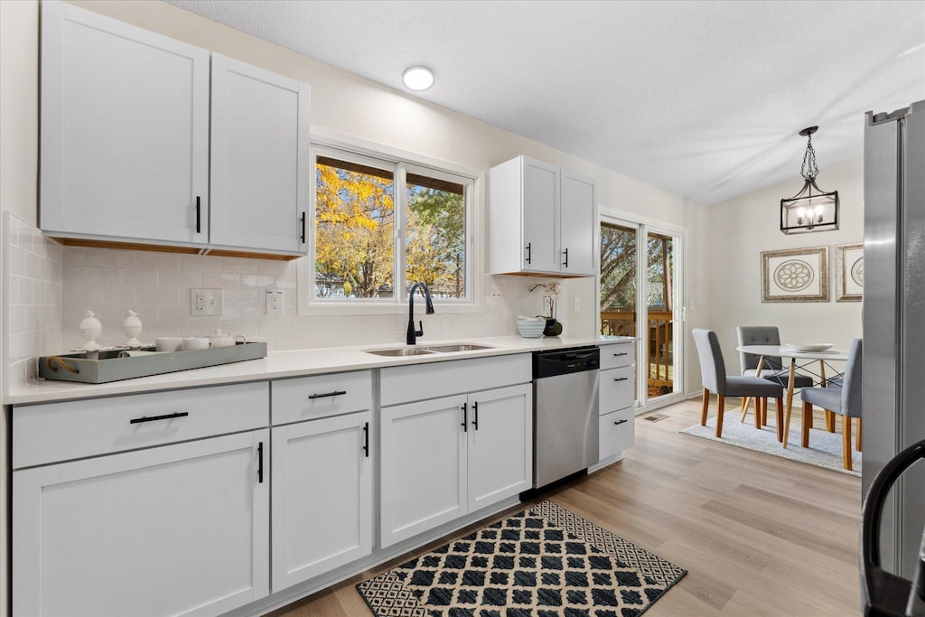 kitchen with sink, white cabinetry, decorative light fixtures, light wood-type flooring, and appliances with stainless steel finishes