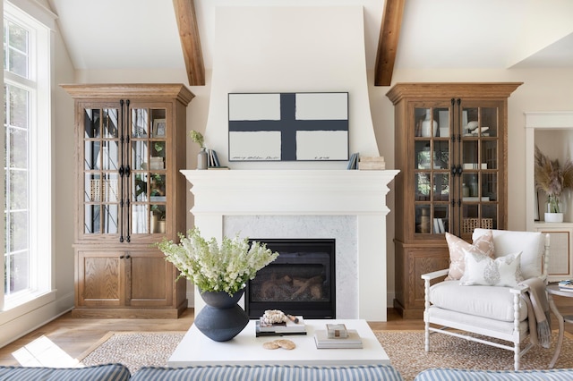 living room with a premium fireplace, vaulted ceiling with beams, a wealth of natural light, and light wood-type flooring