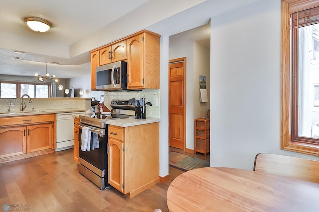 kitchen featuring appliances with stainless steel finishes, sink, decorative backsplash, hanging light fixtures, and hardwood / wood-style flooring