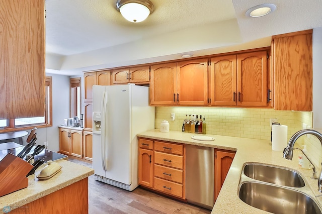 kitchen with sink, tasteful backsplash, a textured ceiling, white refrigerator with ice dispenser, and light hardwood / wood-style floors