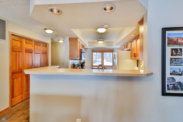 kitchen with fridge, kitchen peninsula, a textured ceiling, and light wood-type flooring