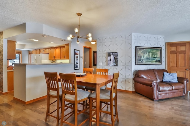 dining space featuring an inviting chandelier, light hardwood / wood-style floors, and a textured ceiling