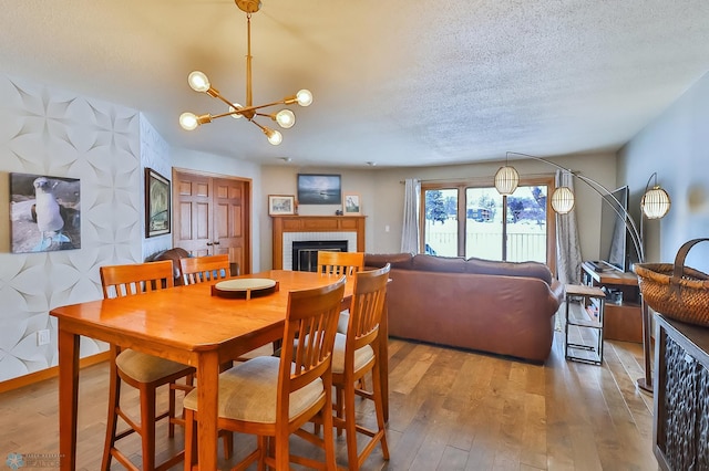 dining room featuring wood-type flooring, a fireplace, a textured ceiling, and a notable chandelier