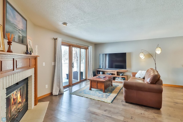 living room with a brick fireplace, a textured ceiling, and light hardwood / wood-style flooring