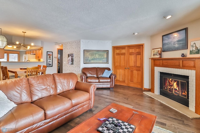 living room featuring a brick fireplace, dark wood-type flooring, a chandelier, and a textured ceiling