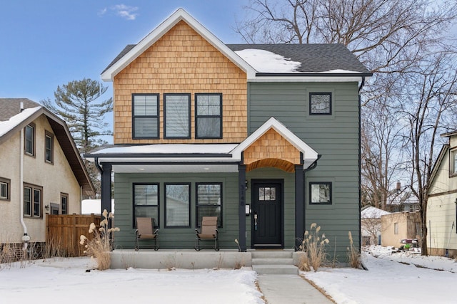 view of front of home with covered porch, a shingled roof, and fence