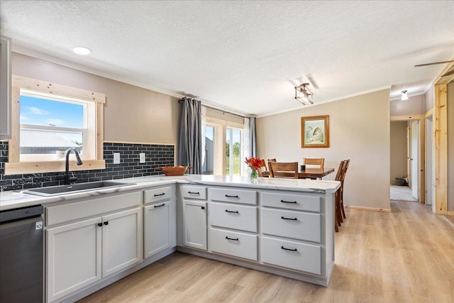 kitchen featuring light wood-style flooring, a sink, tasteful backsplash, light countertops, and dishwasher