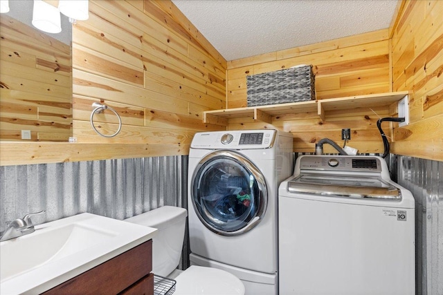 washroom with a sink, wooden walls, laundry area, and washer and clothes dryer