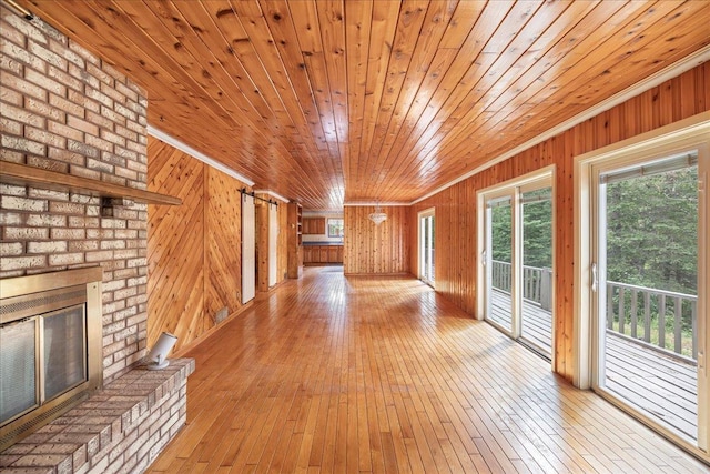 unfurnished living room with wooden walls, light hardwood / wood-style floors, a brick fireplace, and wooden ceiling