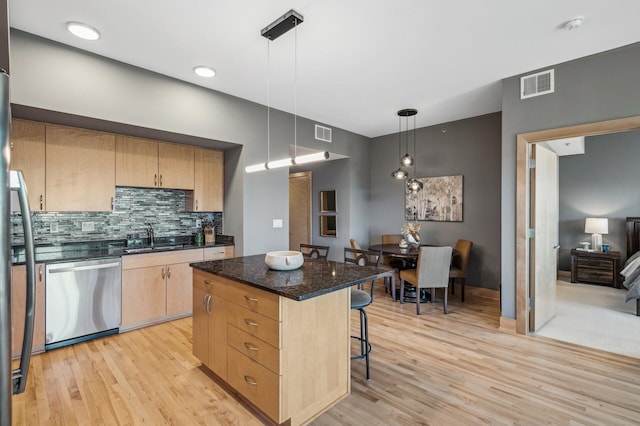 kitchen with visible vents, dishwasher, a breakfast bar area, light brown cabinetry, and a sink