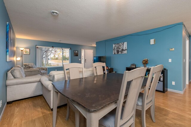 dining space with a textured ceiling, light wood-type flooring, and baseboards