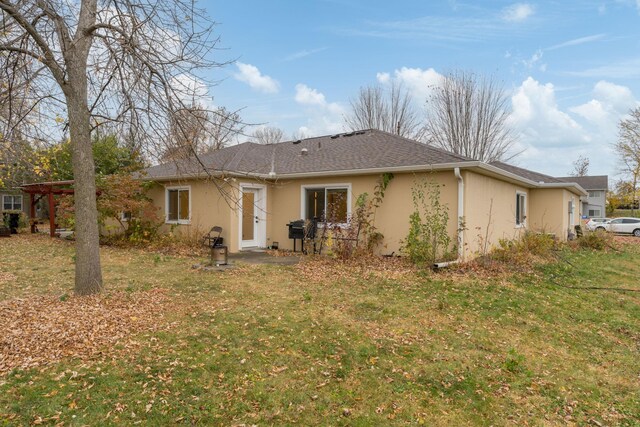 back of property featuring stucco siding, a shingled roof, and a yard