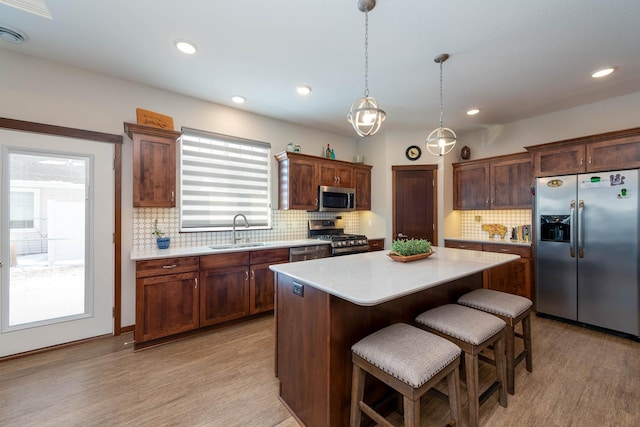 kitchen featuring sink, a center island, hanging light fixtures, light wood-type flooring, and stainless steel appliances